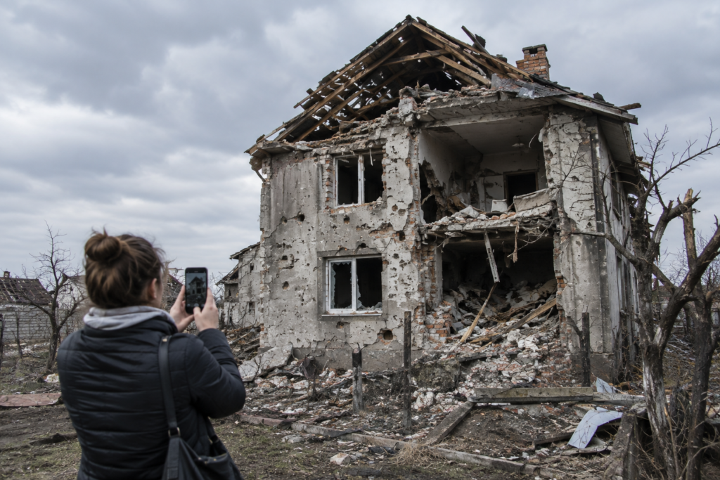 Пошкоджений будинок через війну, людина фотографує руйнування