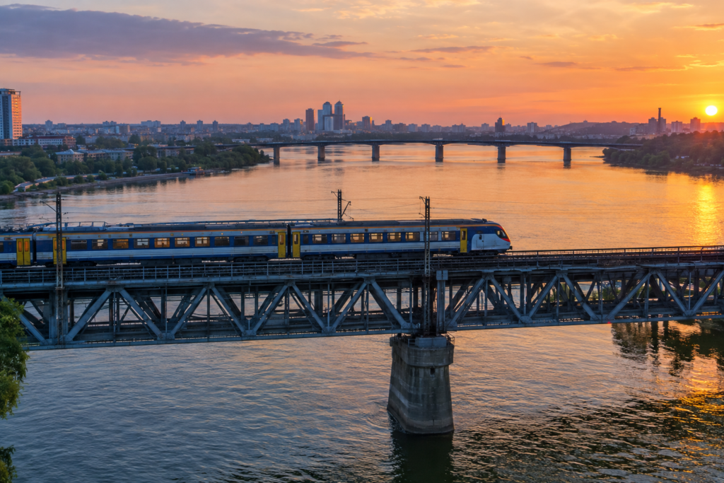 Регіональний потяг переправляється через Дніпро, на тлі видимі мости